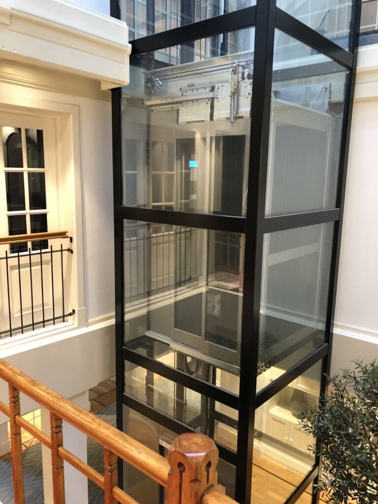 Glazen cabinelift met zwart stalen frame geïnstalleerd in klassiek kantoorpand in Rotterdam