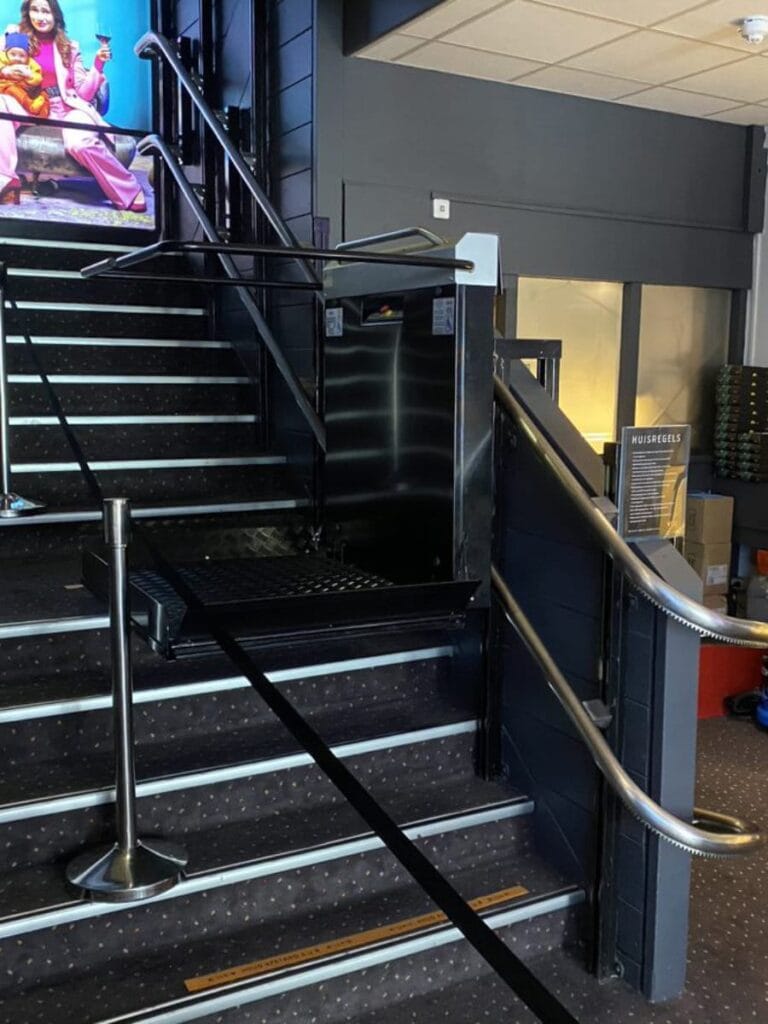 Plateautraplift in zwarte uitvoering geïnstalleerd naast de trap in Vue Cinema Alphen aan den Rijn