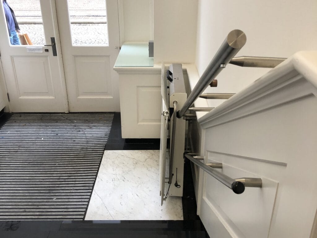 Ingeklapte plateautraplift op de trap bij de entree van De Groote Club in Amsterdam