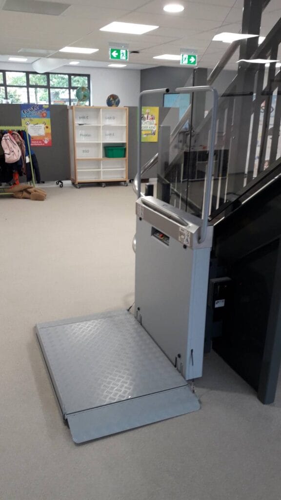 Plateautraplift geïnstalleerd naast een glazen trap in een basisschool