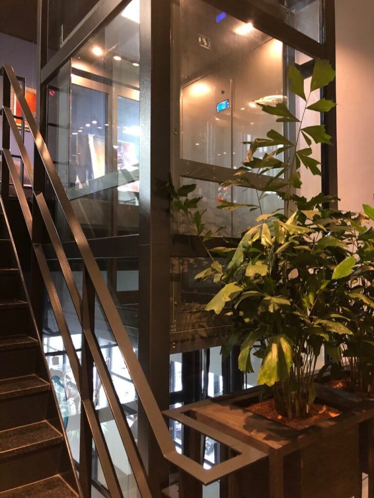 Glazen cabinelift naast een stalen trap in restaurant Finder Relais Amsterdam