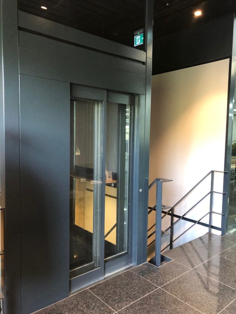 Donkergrijze cabinelift met glazen deuren in de moderne entreehal van Finder Relais Amsterdam