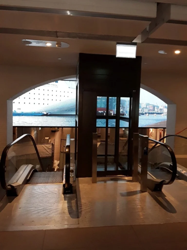 Cabinelift met donker metalen frame geplaatst naast roltrappen in een havengebouw in Amsterdam