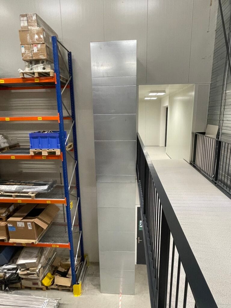Goederenlift met roestvrijstalen koker geïnstalleerd naast magazijnstellingen in bedrijfspand Pall Medistad Medemblik