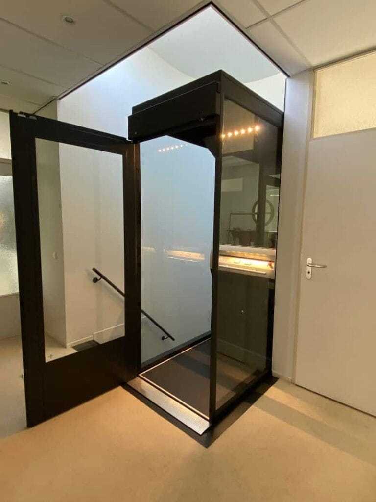 Glazen cabinelift met donker aluminium frame geplaatst in een moderne kantooromgeving