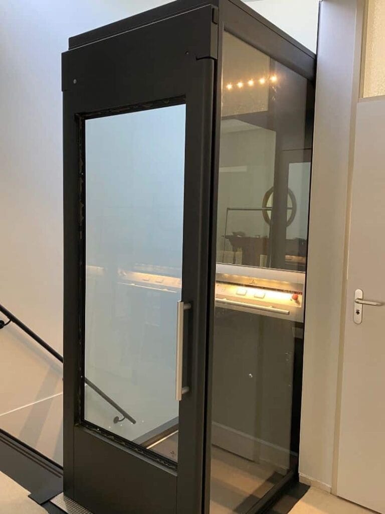 Zwarte glazen woonhuislift geplaatst naast een trap in een modern woonhuis