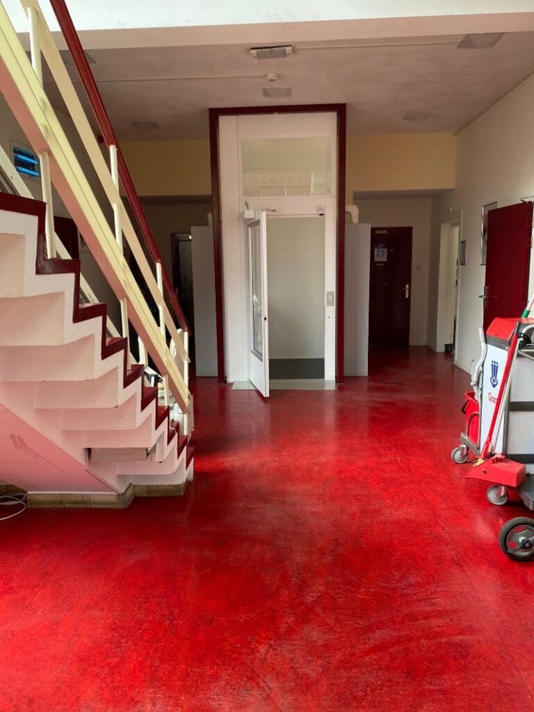 Cabinelift in de hal van een stichting in Hilversum naast een trap met rode vloer