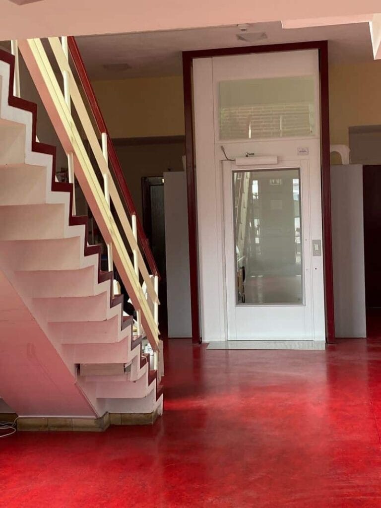 Platformlift met glazen deur naast een trap in een gebouw van een stichting in Hilversum