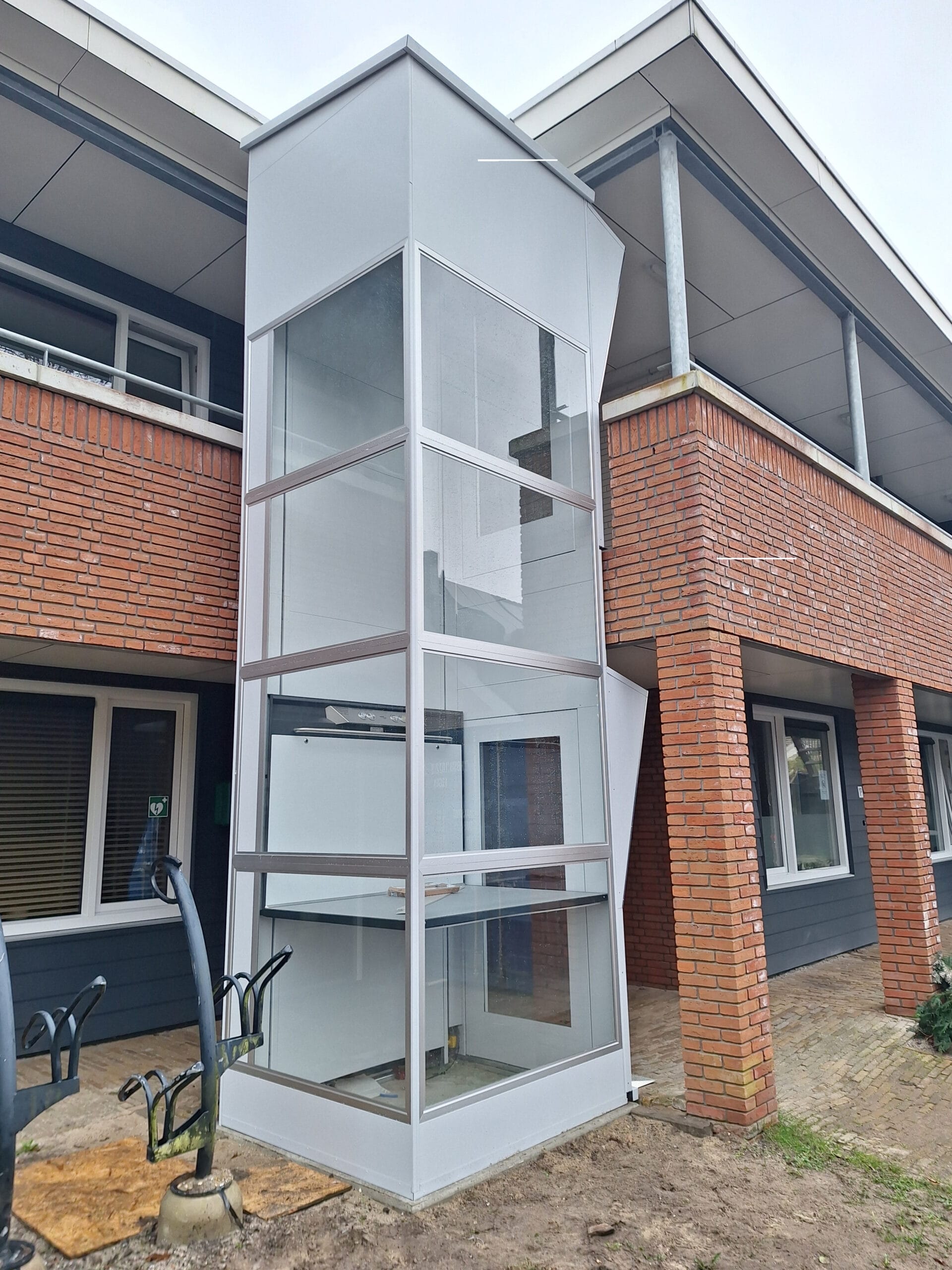 Glazen platformlift aan de buitengevel van een appartementencomplex in Heiloo of Bergen