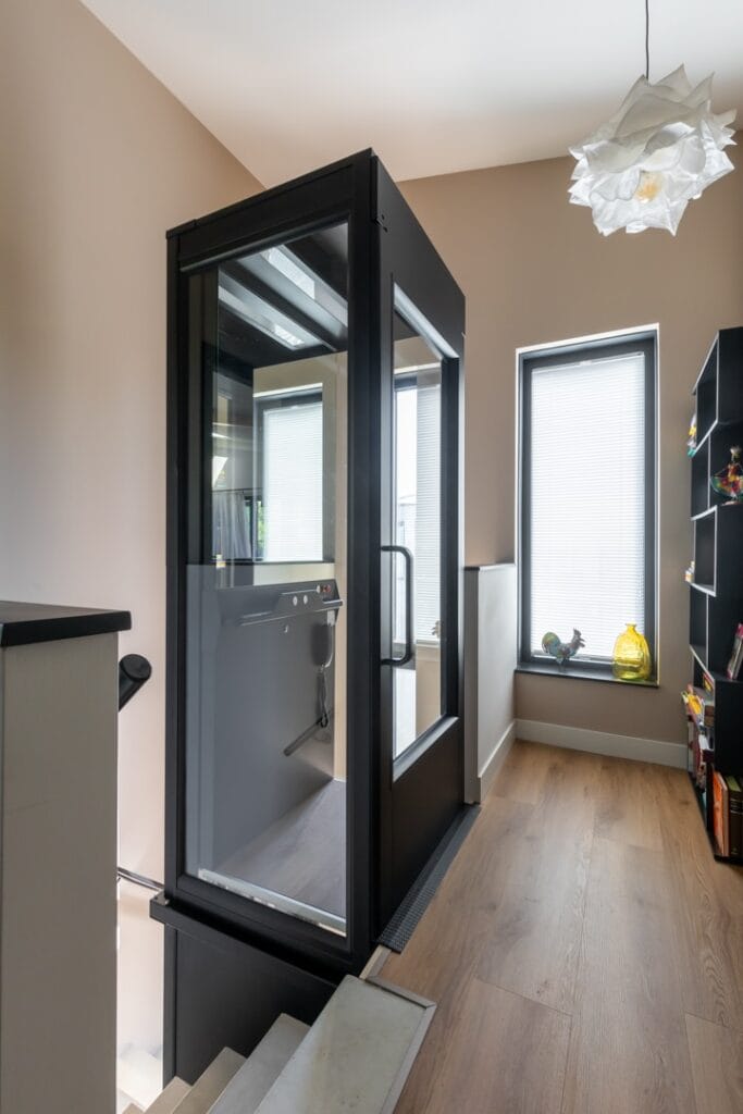 Glazen woonhuislift met zwart frame geplaatst in moderne woning in Roelofarendsveen