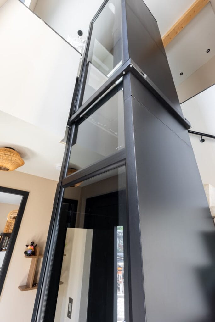 Zwarte woonhuislift met glazen wanden gefotografeerd vanuit lage hoek in woonhuis Roelofarendsveen