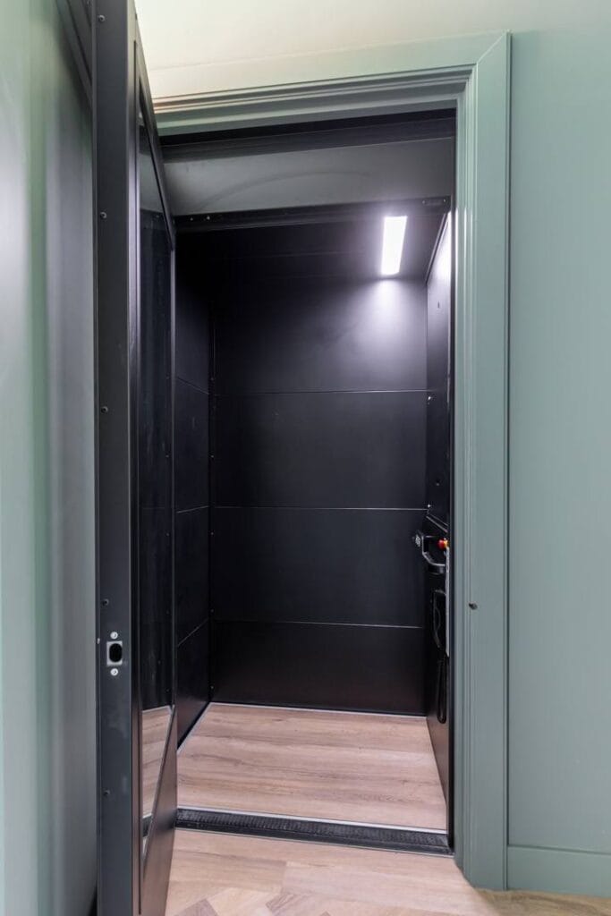 Zwarte cabinelift met open deur in een woonhuis in Den Haag met saliegroen interieur
