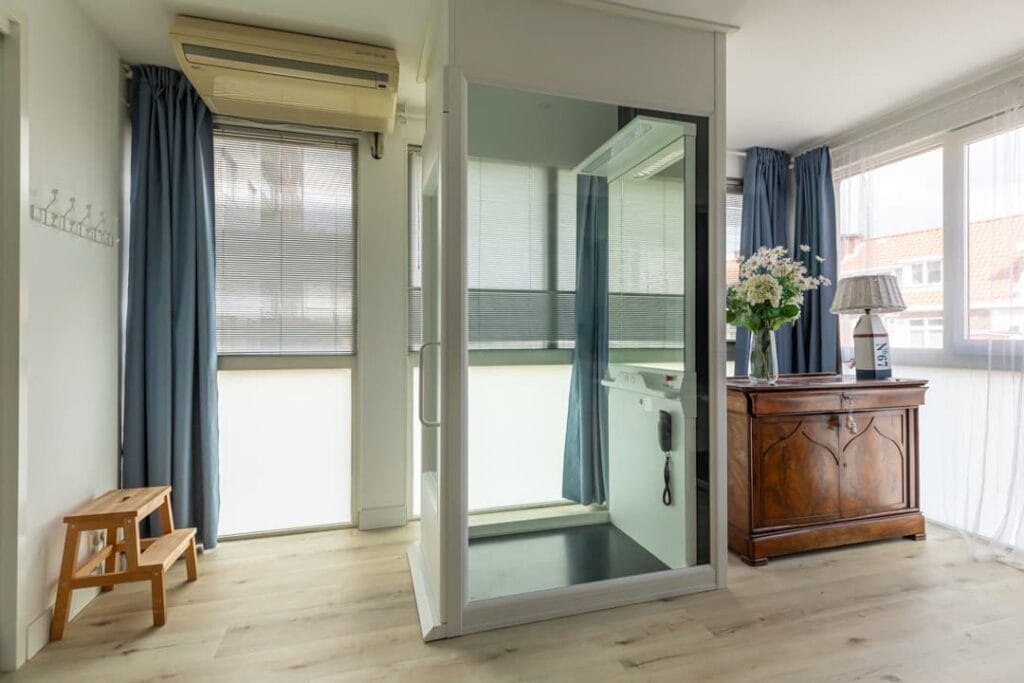 Glazen woonhuislift in lichte woonkamer met houten vloer en blauwe gordijnen in Scheveningen