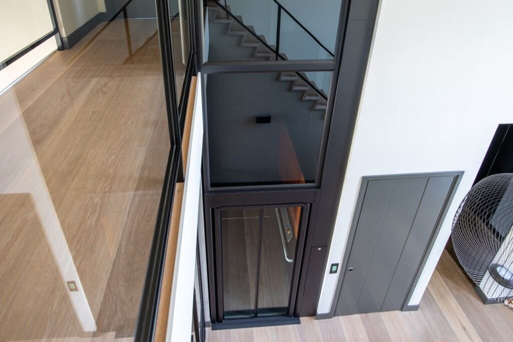 Donkere woonhuislift met glazen cabine gezien vanuit vogelperspectief naast een trap