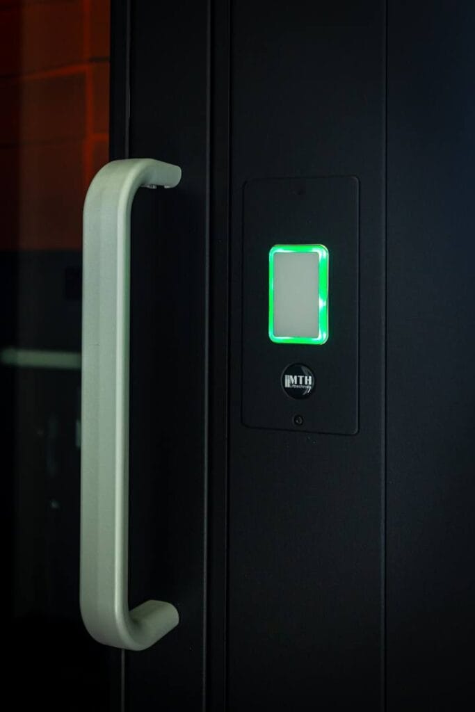 Verlichte oproepknop met MTH-logo op zwarte liftdeur in woonhuis Alphen aan den Rijn
