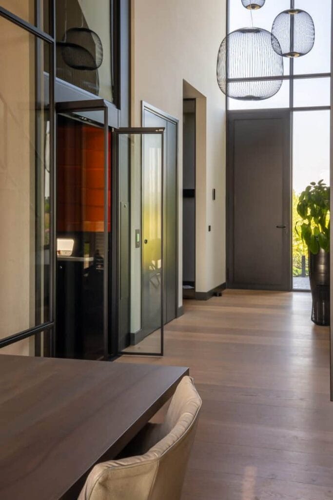 Glazen woonhuislift met oranje cabine-interieur in moderne woning in Alphen aan den Rijn