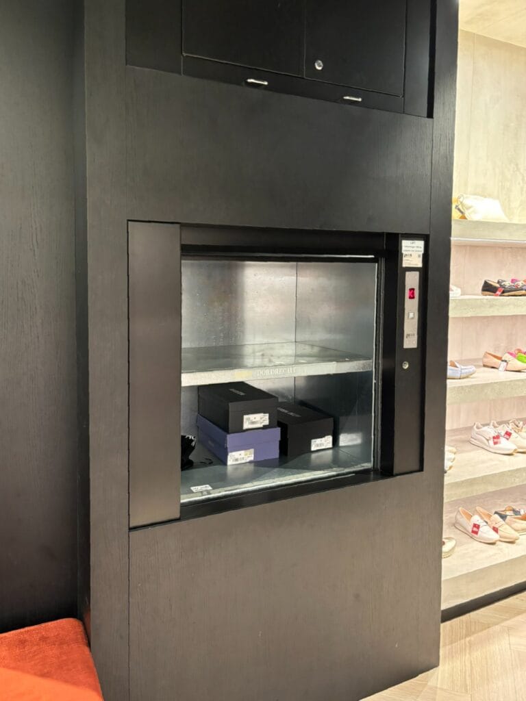 Goederenlift met donker houten ombouw in schoenenwinkel Omoda Dordrecht met schoendozen
