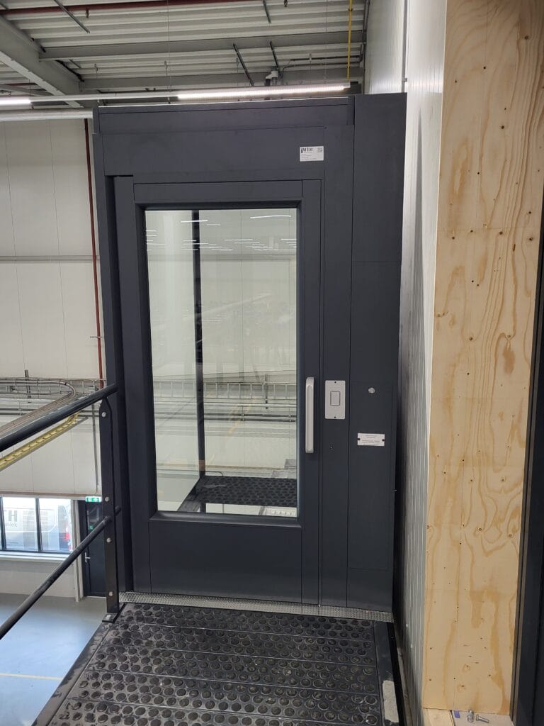 Donkergrijze platformlift met glazen deur geïnstalleerd op mezzanineverdieping bij Ubbink in Doesburg