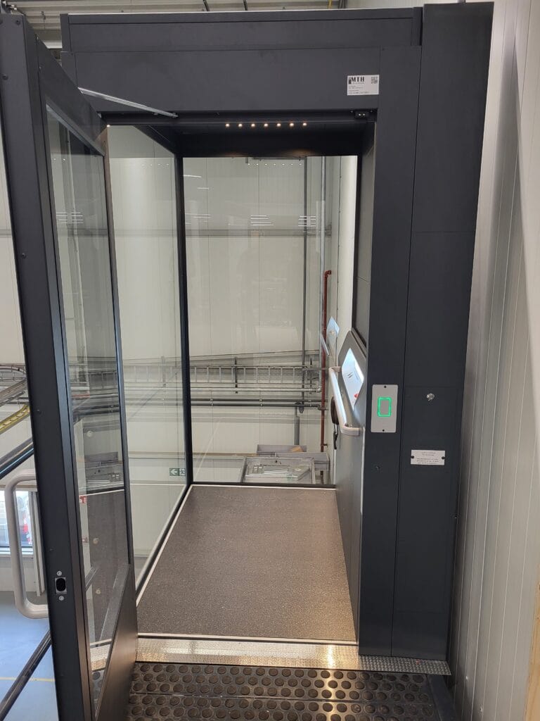 Cabinelift met glazen wanden en zwart frame geïnstalleerd in industriële omgeving bij Ubbink Doesburg