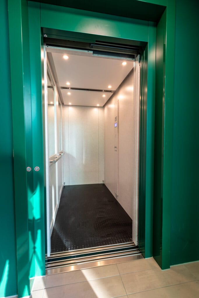 Cabinelift met groene omlijsting en witte cabine in kantoorpand Amsterdam