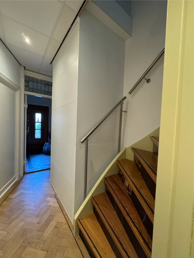 Witte woonhuislift naast houten trap in hal van woning in Den Haag