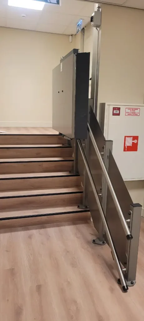 Plateautraplift in RVS-uitvoering gemonteerd naast een houten trap in een zorginstelling in Breda