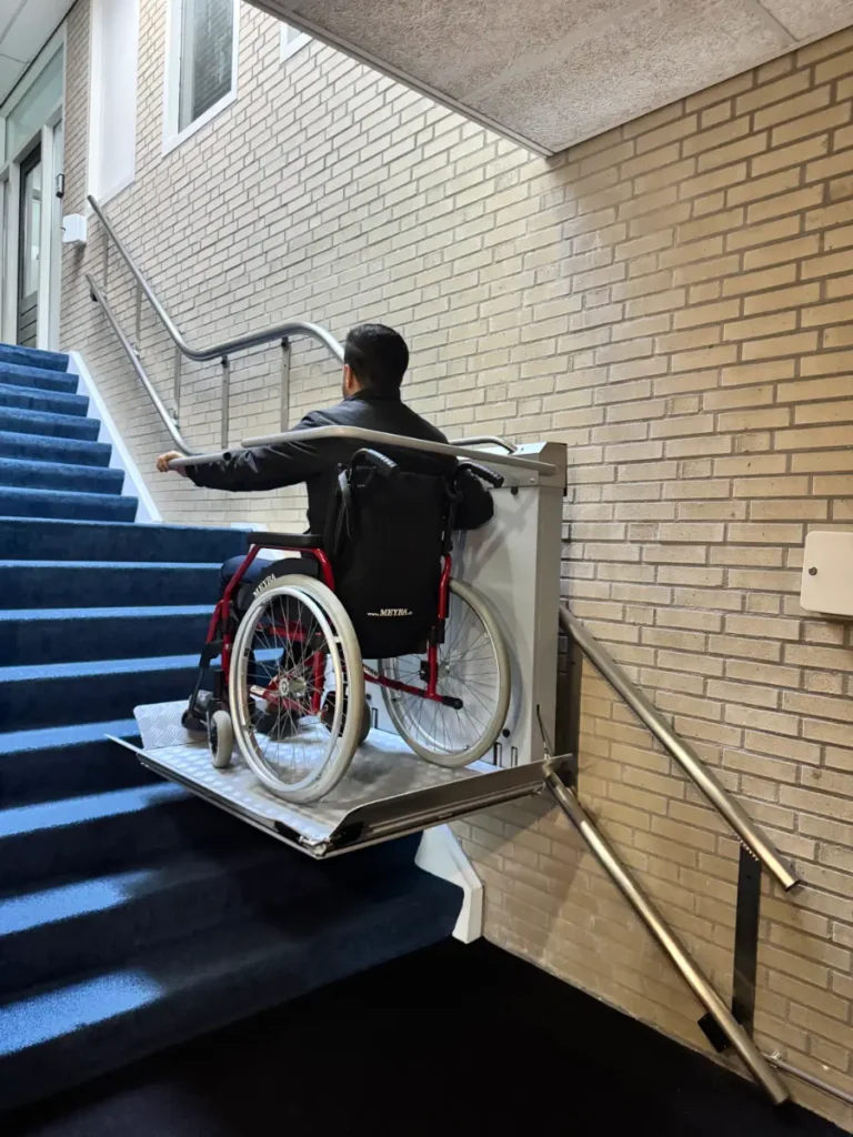 Rolstoelgebruiker rijdt met plateautraplift omhoog langs blauwe trappen in appartementencomplex Roelofarendsveen