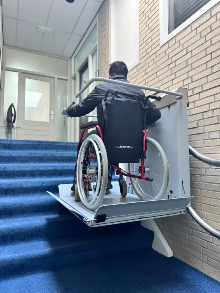 Plateautraplift met rolstoelgebruiker op blauwe trappen in appartementencomplex Roelofarendsveen