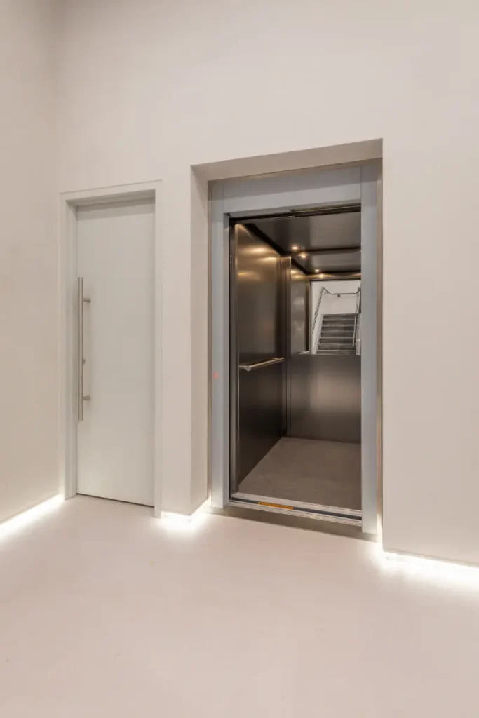 Cabinelift met donkere roestvrijstalen cabine in strak wit interieur van Gymshark Amsterdam