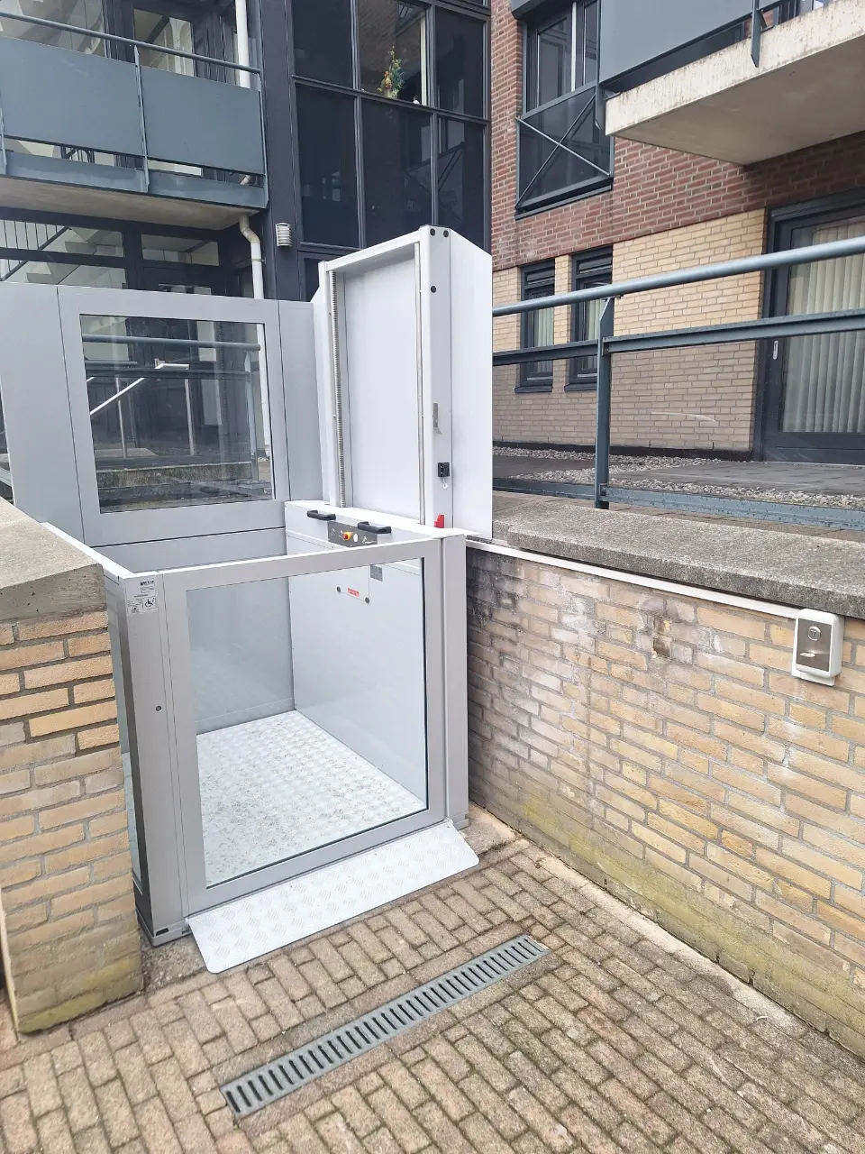 Buitenopgestelde platformlift bij een appartementencomplex in Eindhoven met open glazen cabine