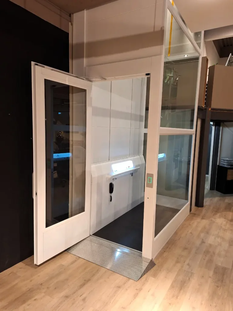 witte platformlift a 7000 met open deur in meubelzaak, voorzien van tranenplaat oprit en verlicht interieur